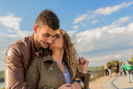 Attractive woman kissing her boyfriend under the bright blue sky