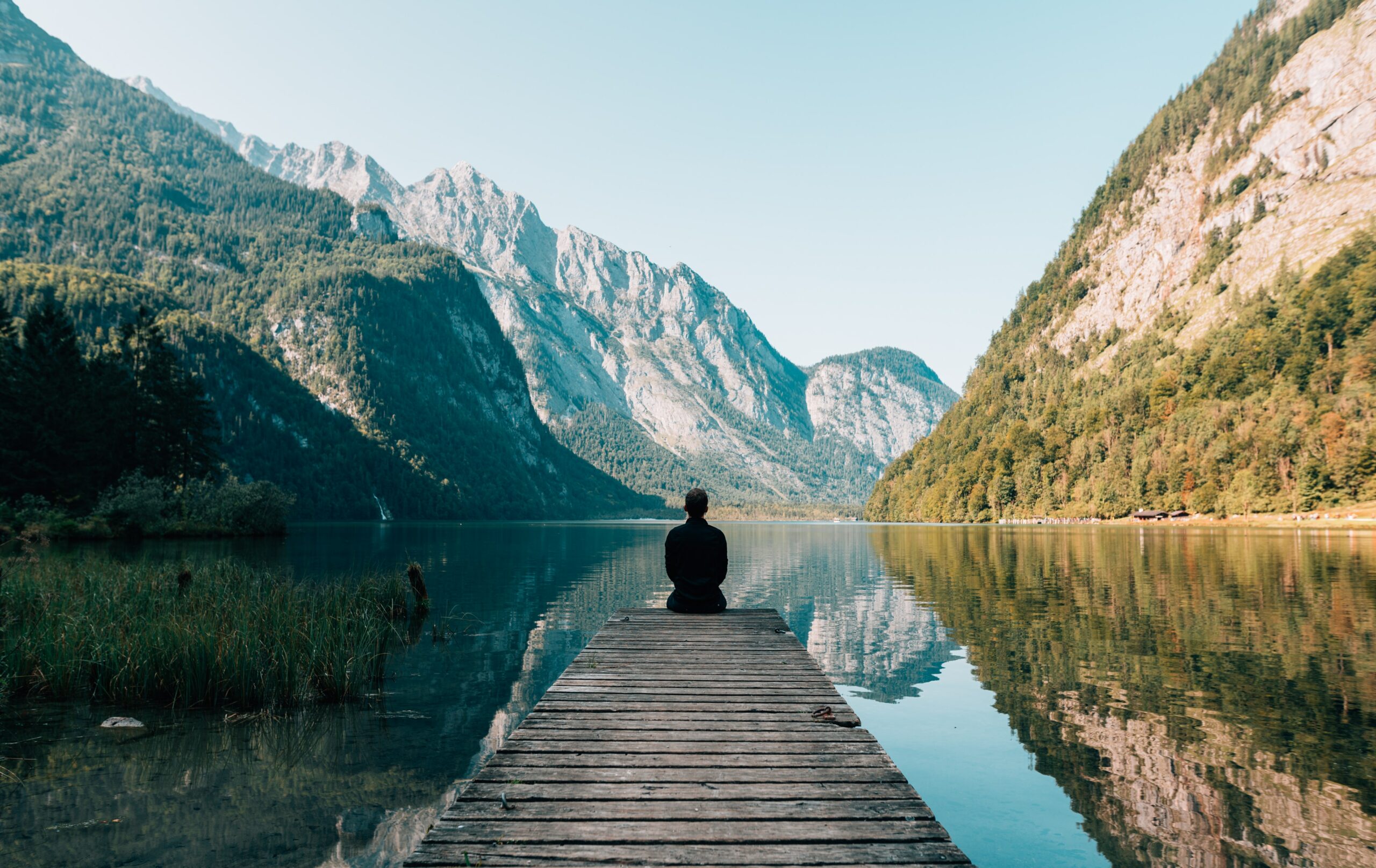 man sitting on boardwalk staring at the mountains and water around him