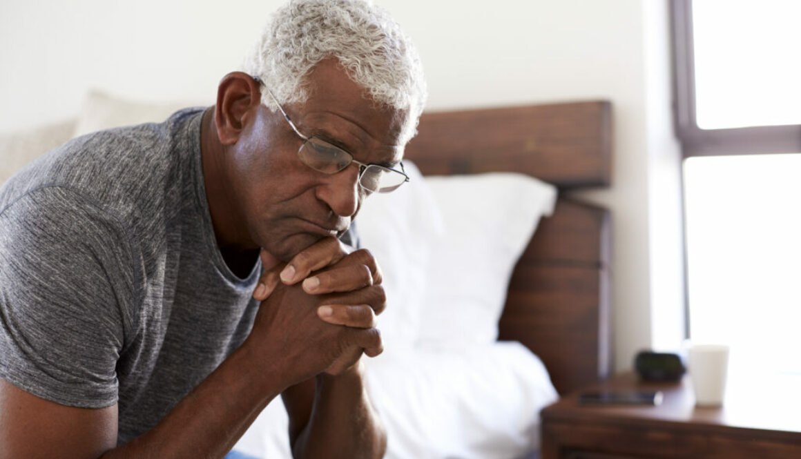 Depressed Senior Man Looking Unhappy Sitting On Side Of Bed At Home With Head In Hands