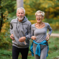 Cheerful active senior couple jogging in the park. Exercise toge