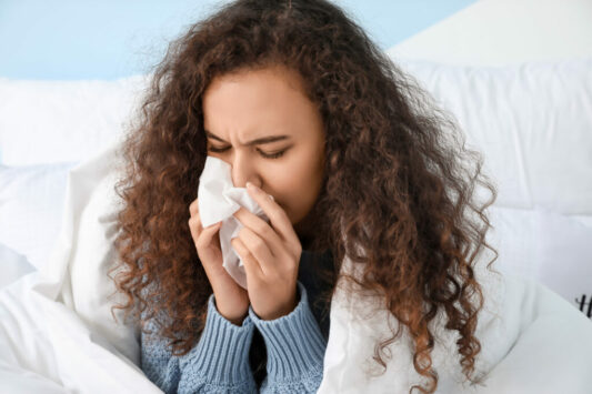 Someone sneezing into a Kleenex tissue what suffering from Covid or flu related symptoms.